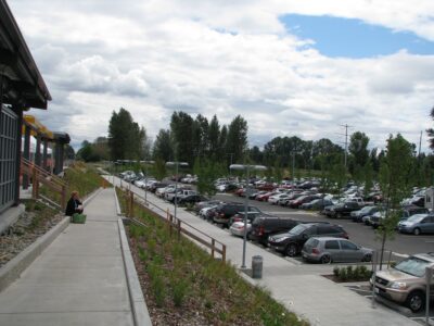 A person sits on a step between the front of the station and the parking lot.