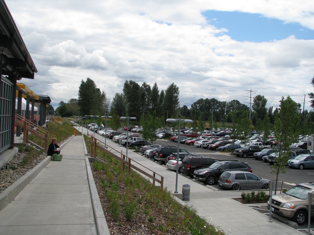 A person sits on a step between the front of the station and the parking lot.