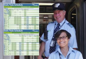 In the foreground is a table showing an example schedule, too small to read. Behind the table are two train employees smiling at the camera.