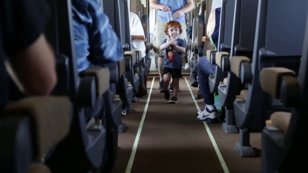 A young child walks down the center aisle of a train car.