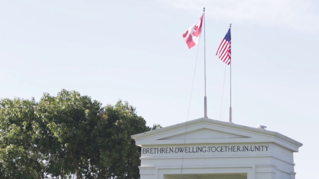 The top of a building that is displaying the Canadian and American flags. Printed on the building are the words "Brethren dwelling together in unity."