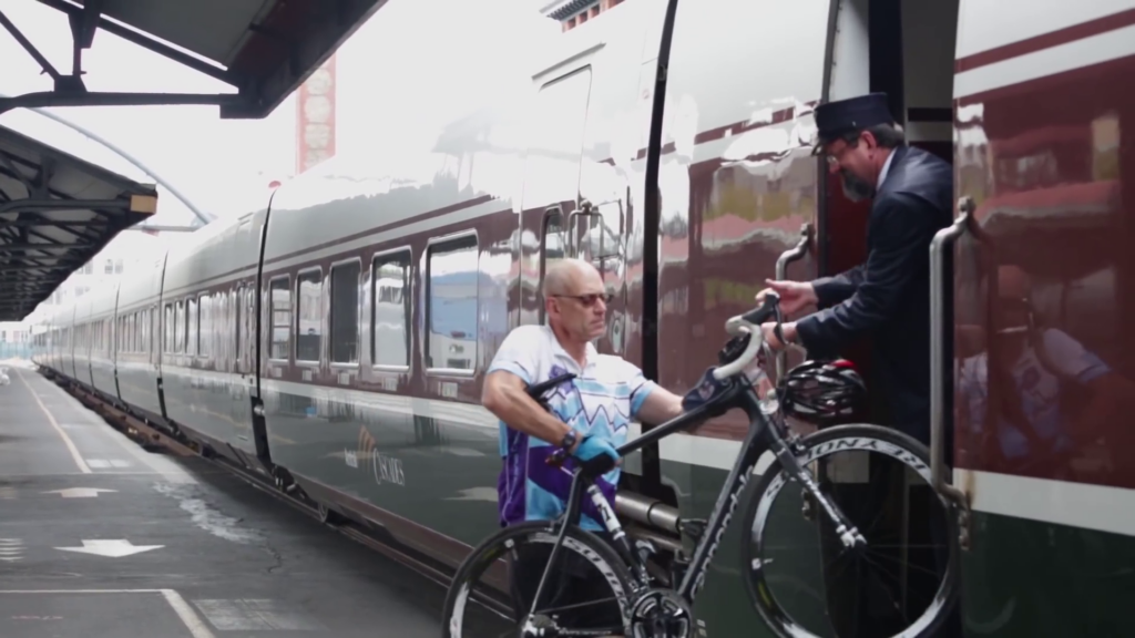 A person wearing bicycle gloves lifts his bicycle up to hand it to a person standing inside a train car.