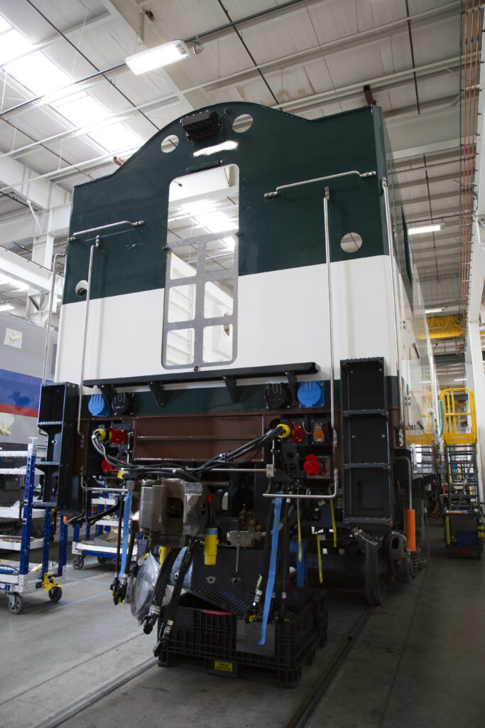 The rear of a train car in a warehouse. The car is a dark green with white accents.