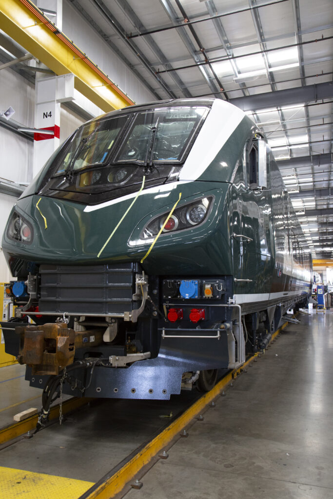 The front of a train car in a warehouse. The car is a dark green with white accents.