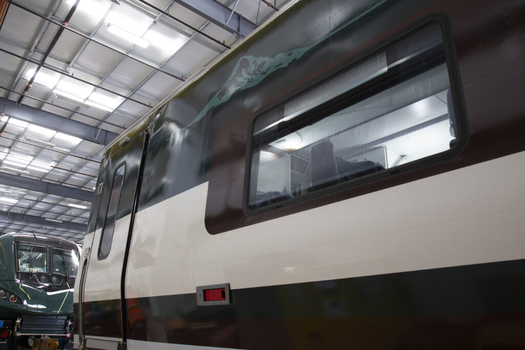 The side of a train car in a warehouse. The car is a dark green with white accents.