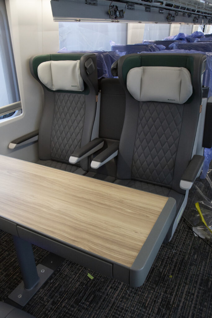 Two seats in the interior of the train. The head rest has text printed on it that says "Business." There is a table in front of the two seats.